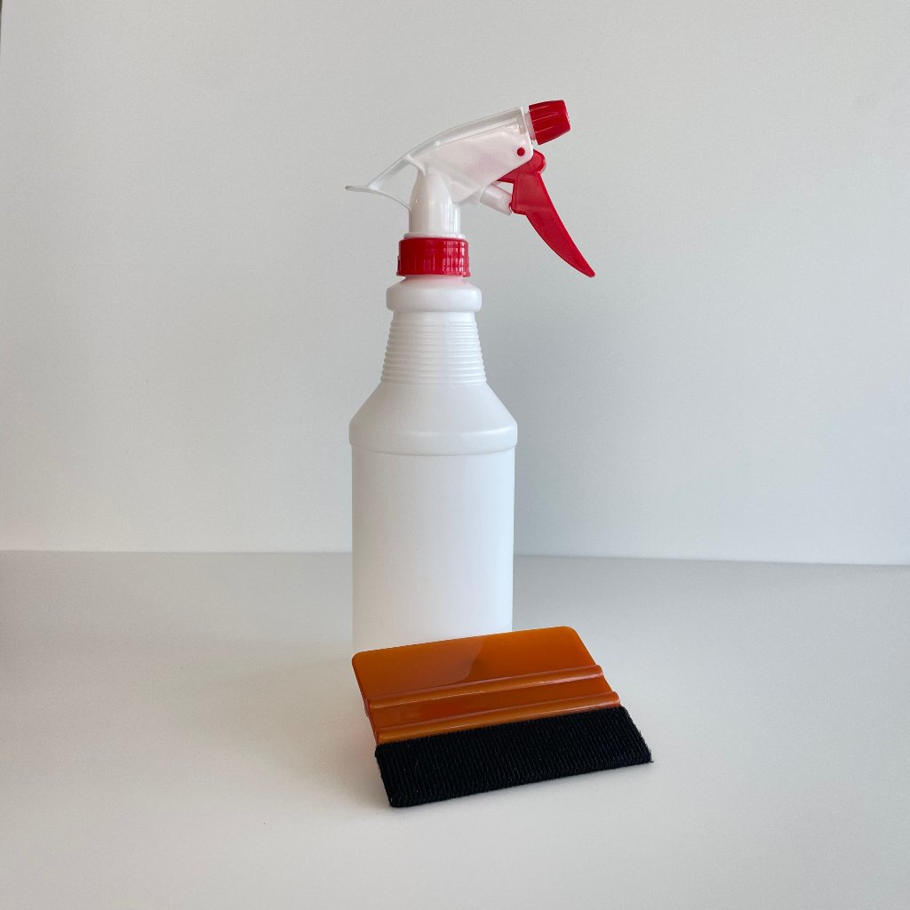 Hvid sprayflaske med rød udløser og orange skraber med sort filt kant.