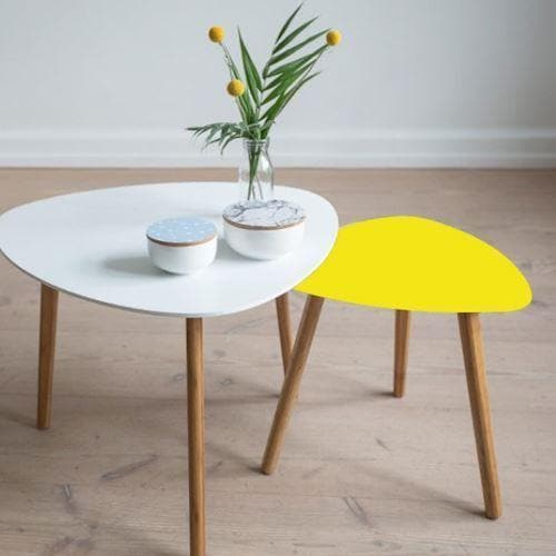 To borde i træ. Det ene er hvidt, det andet med gul top. Vase med blomster og skåle på det hvide bord.