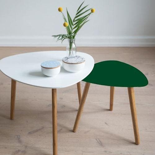 Lille bord med mørkegrøn folie ved hvidt bord. Begge har træben og står på lyst trægulv.