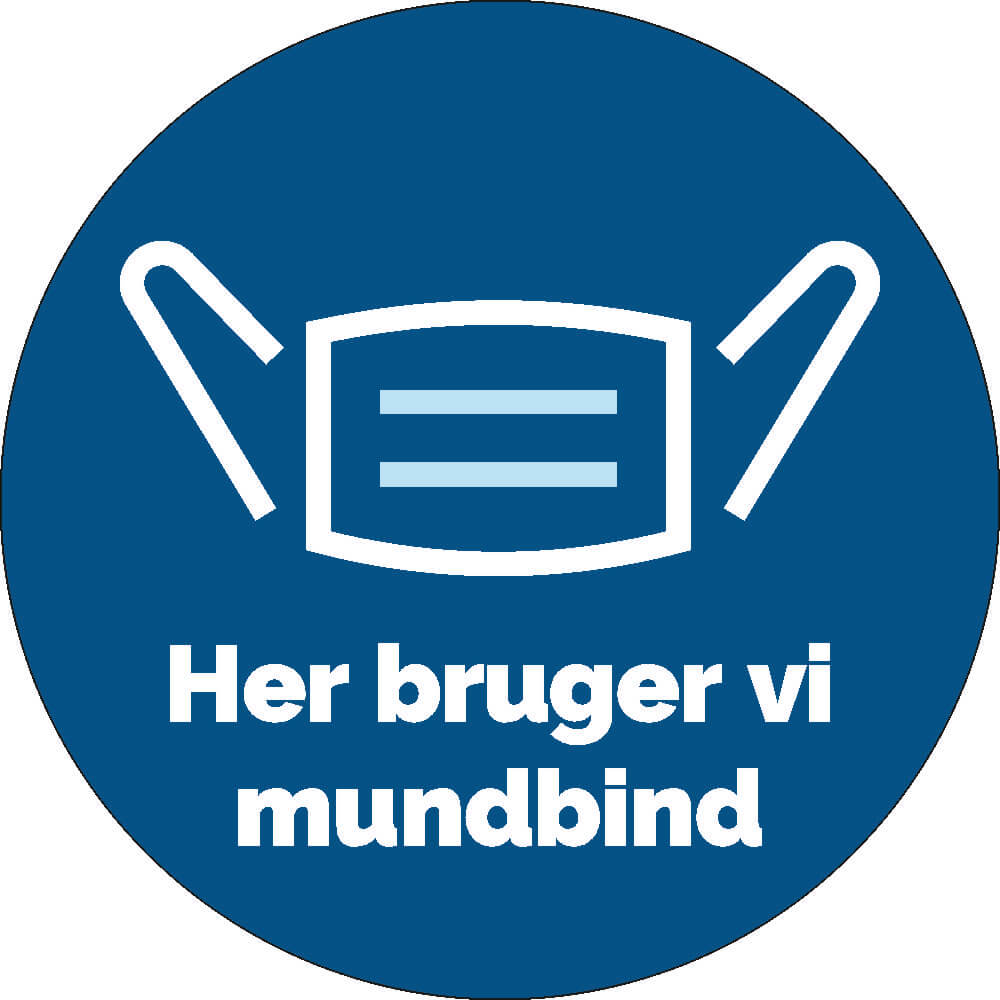 Rundt gulvklistermærke med blå baggrund, hvidt mundbindgrafik og teksten "Her bruger vi mundbind".