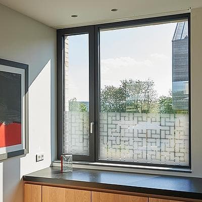 Vindue med sandblæst film i geometrisk mønster, der giver privatliv og slipper lys ind.