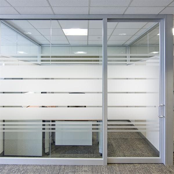 Glasvæg med sandblæst design og vandrette striber i kontormiljø, inkl. dør.