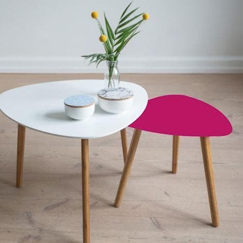 To borde med træben, et pink og et hvidt med vase og skåle på trægulv.