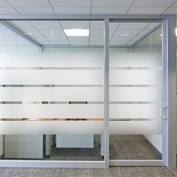 Kontor med glasvægge og sandblæste horisontale striber, der giver privatliv og lysindfald.